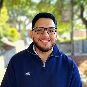 Close-up of Mark Perez-Navarro, who has short black hair and a beard. Perez-Navarro wears glasses and a blue jacket.